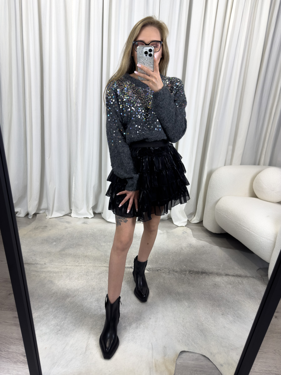 Sweter Sequins ciemny szary z okrągłym dekoltem, błyszczącymi cekinami i klasycznym fasonem, zestawiony z czarną spódnicą mini z falbanami – elegancka stylizacja na zimowy wieczór.