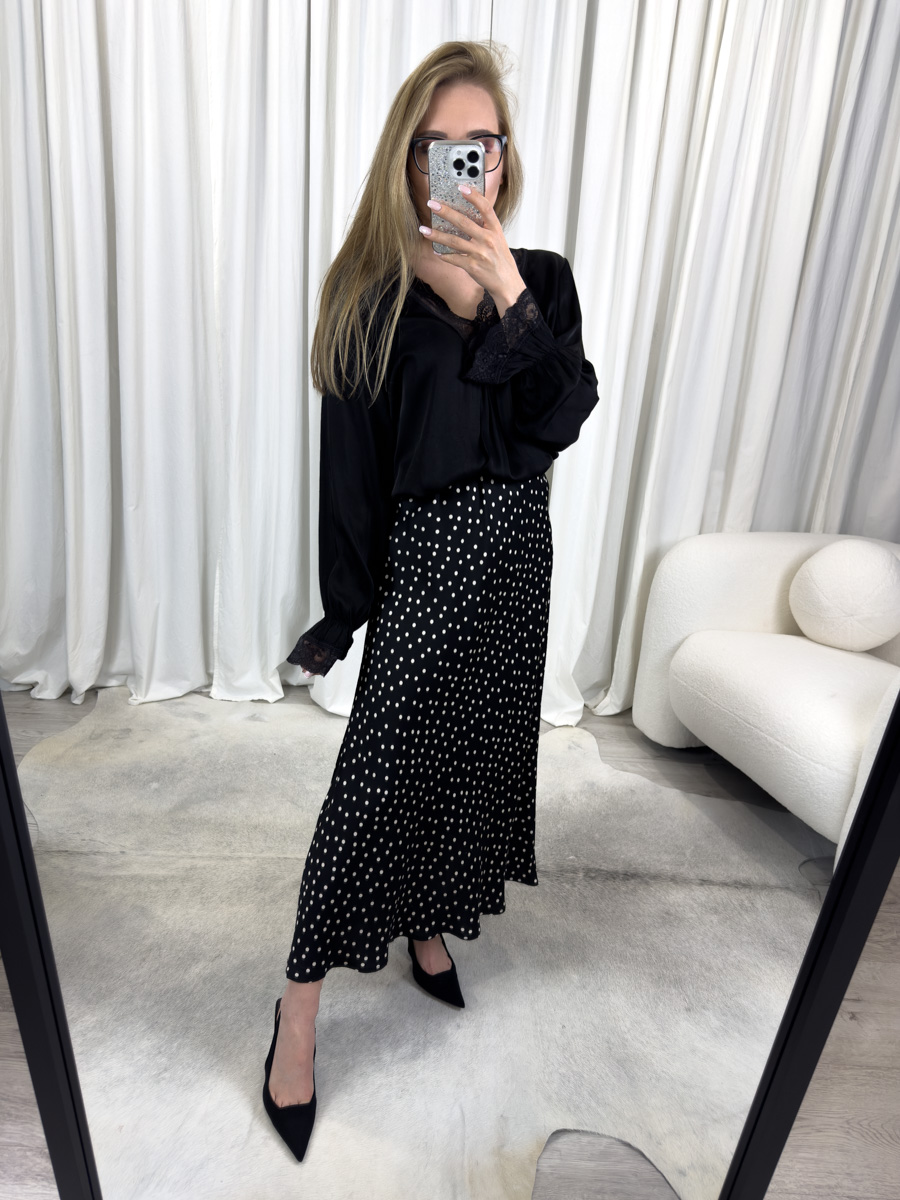 Spódnica Dots o długości midi, w klasyczny wzór w groszki, zestawiona z czarną koszulą z koronką – elegancka i uniwersalna stylizacja na co dzień i na wyjątkowe okazje.