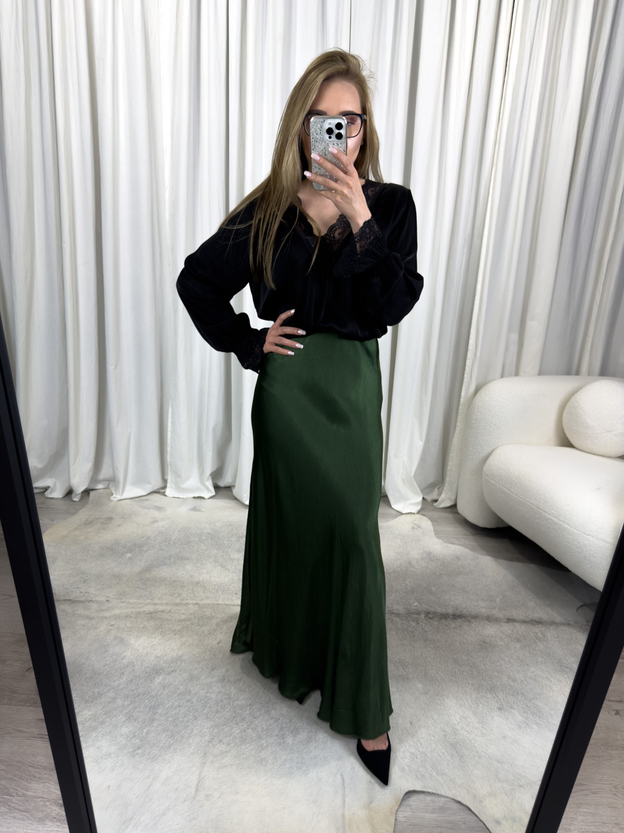 Spódnica Satine Green o długości maxi w szmaragdowym odcieniu, wykonana z połyskującej satyny, zestawiona z czarną bluzką – elegancka stylizacja idealna na wieczór lub specjalne okazje.