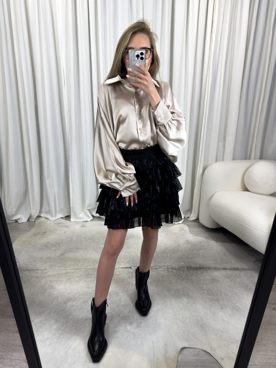 Koszula oversize Mia z satyny w odcieniu szampańskim, z klasycznym kołnierzykiem i mankietami, zestawiona z czarną spódnicą mini z falbanami – elegancka stylizacja z nutą luzu.