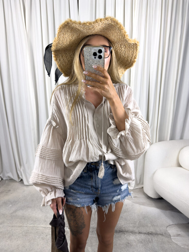 Zdjęcie produktowe sklepu internetowego z odzieżą damską – modelka ubrana w koszule Boho w kolorze beżowym marki Wiya, jeansowe szorty oraz dodatki typu słomiany kapelusz, zamszowa torebka shoperka