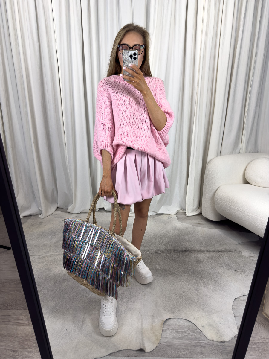 Kobieta w krótkim pastelowym swetrze oversize Shorty Pink, różowej spódniczce i białych sneakersach, trzymająca torbę z frędzlami – dziewczęca stylizacja na lato