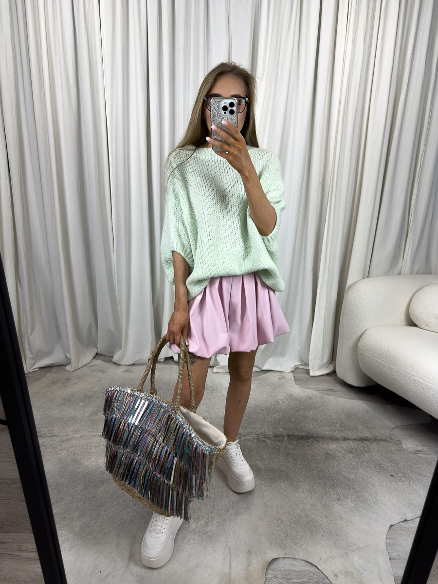 Kobieta w krótkim pastelowym swetrze oversize Shorty Mint, różowej spódniczce i białych sneakersach, trzymająca torbę z frędzlami – stylizacja w stylu pastel streetwear