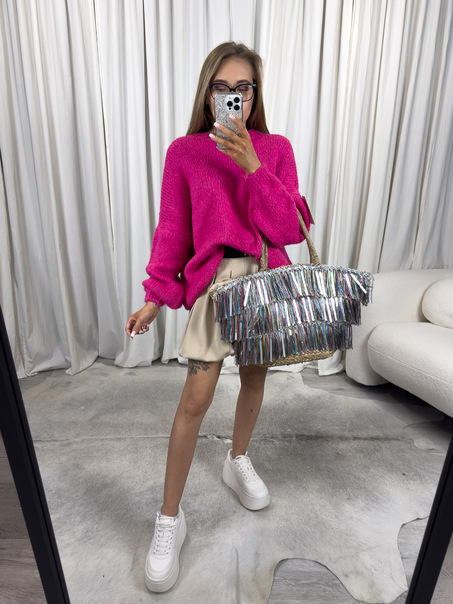 Kobieta w fuksjowym swetrze oversize Balloon i plisowanej spódnicy, trzymająca kolorową torbę – stylizacja w miejskim stylu.