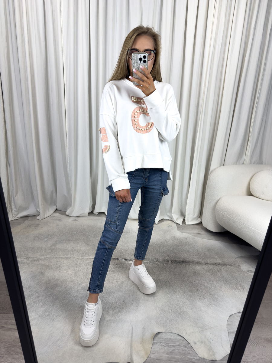 Modelka w białej bluzie z perełkami White, jeansach skinny i białych sneakersach – stylizacja casual z eleganckim akcentem.