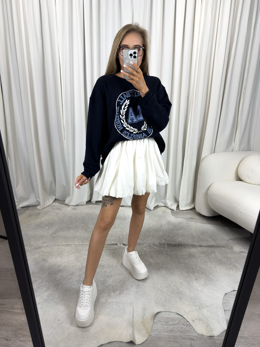 Bluza oversize College granatowa z nadrukiem college, stylizacja z białą spódnicą i białymi sneakersami, zdjęcie produktowe na tle jasnych zasłon.
