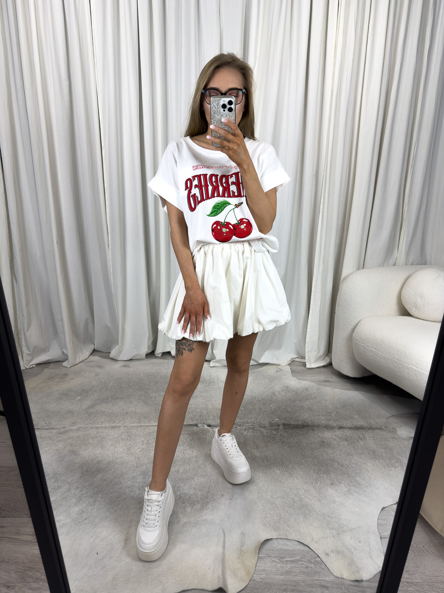 T-shirt z nadrukiem wiśni w kolorze białym w stylizacji z krótką białą spódniczką – letnia stylizacja casual z owocowym akcentem.