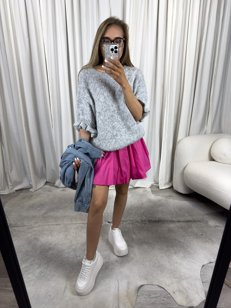 Sweter pastelowy Flounce w kolorze szarego melanżu zestawiony z różową spódniczką i białymi sneakersami – stylizacja na co dzień.