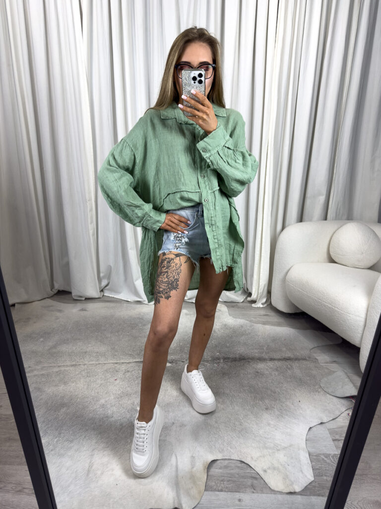 Zielona lniana koszula Lori Wiya - asymetryczny krój oversize, naturalny len i luźny fason. Stylizacja z niebieskimi, jeansowymi szortami.