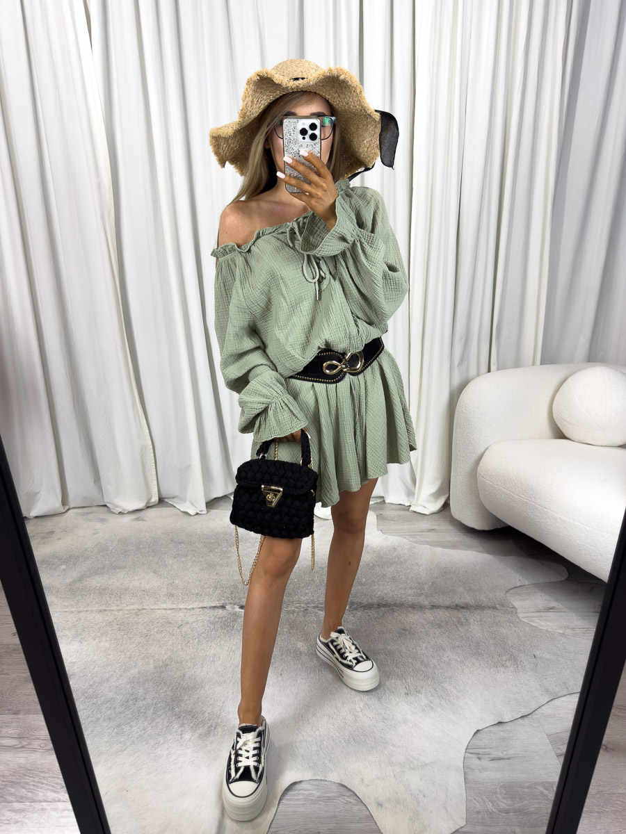 Modelka w kombinezonie muślinowym Safari z odkrytym ramieniem, wiązaniem na dekolcie i szerokim paskiem w talii. Zdjęcie produktowe sklepu internetowego z odzieżą damską.