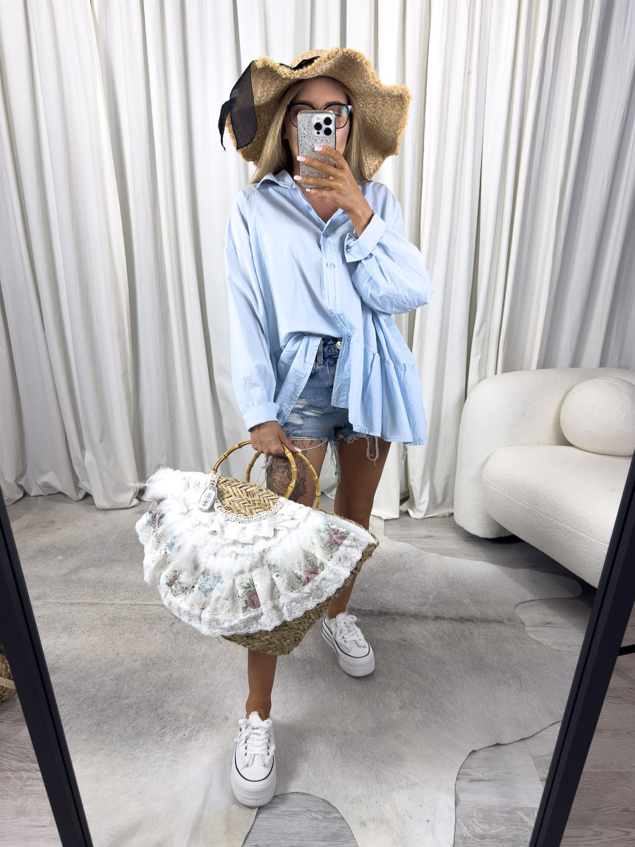 Zdjęcie produktowe sklepu internetowego z odzieżą damską – modelka w błękitnej koszuli Fiamma Gioya z falbaną, jeansowych szortach i dużej wiklinowej torbie