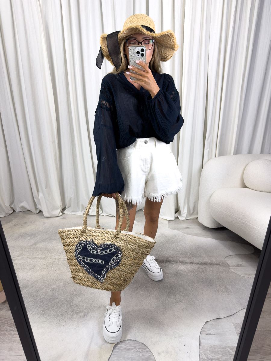 Zdjęcie produktowe sklepu internetowego z odzieżą damską – modelka w koszuli Malta Wiya granatowej, białych szortach z frędzlami, wiklinowej torbie i kapeluszu