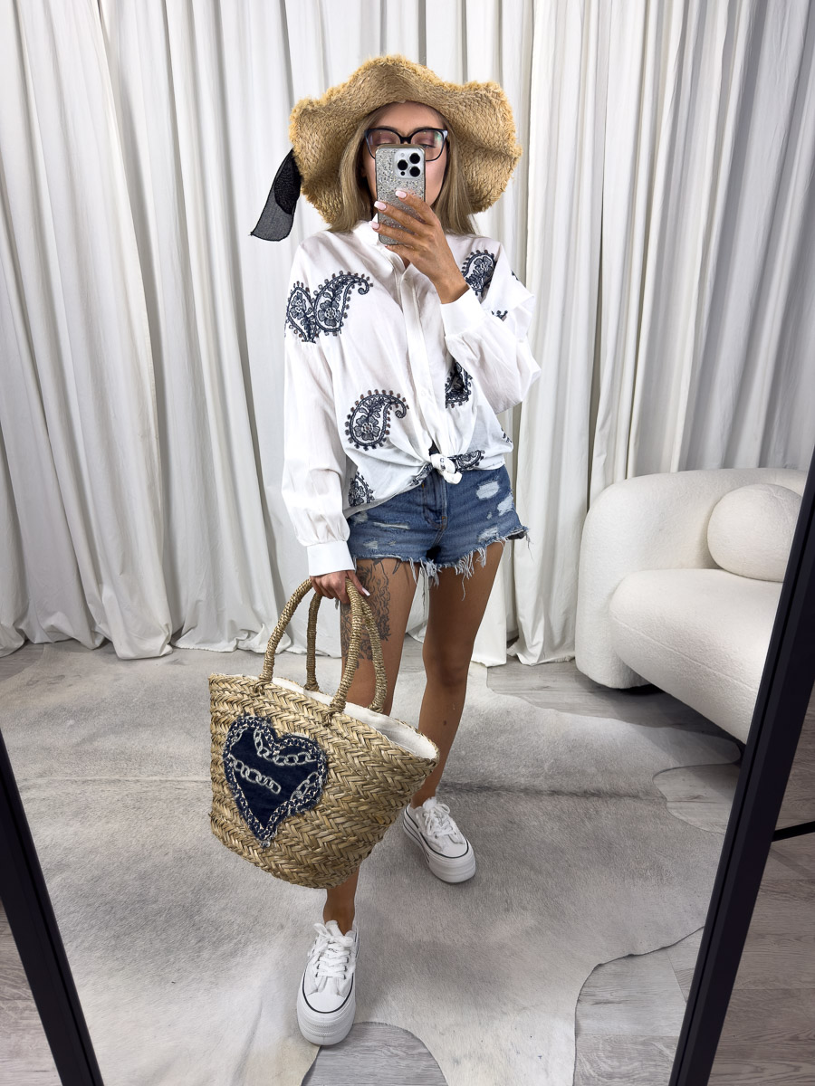 Zdjęcie produktowe sklepu internetowego z odzieżą damską – modelka w koszuli Ricamato granatowej z haftem etno, zawiązanej w pasie, jeansowych szortach i wiklinowej torbie