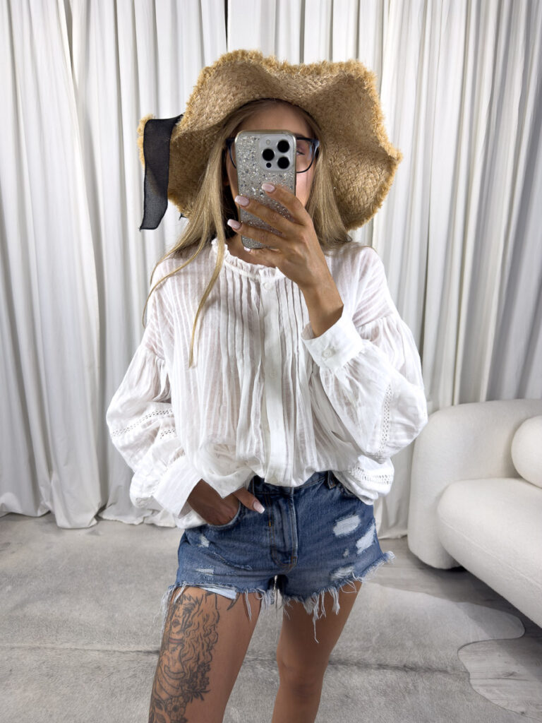 Zdjęcie produktowe sklepu internetowego z odzieżą damską – modelka w koszuli boho Luna marki Wiya, zestawionej z jeansowymi szortami, kapeluszem i wiklinową torbą