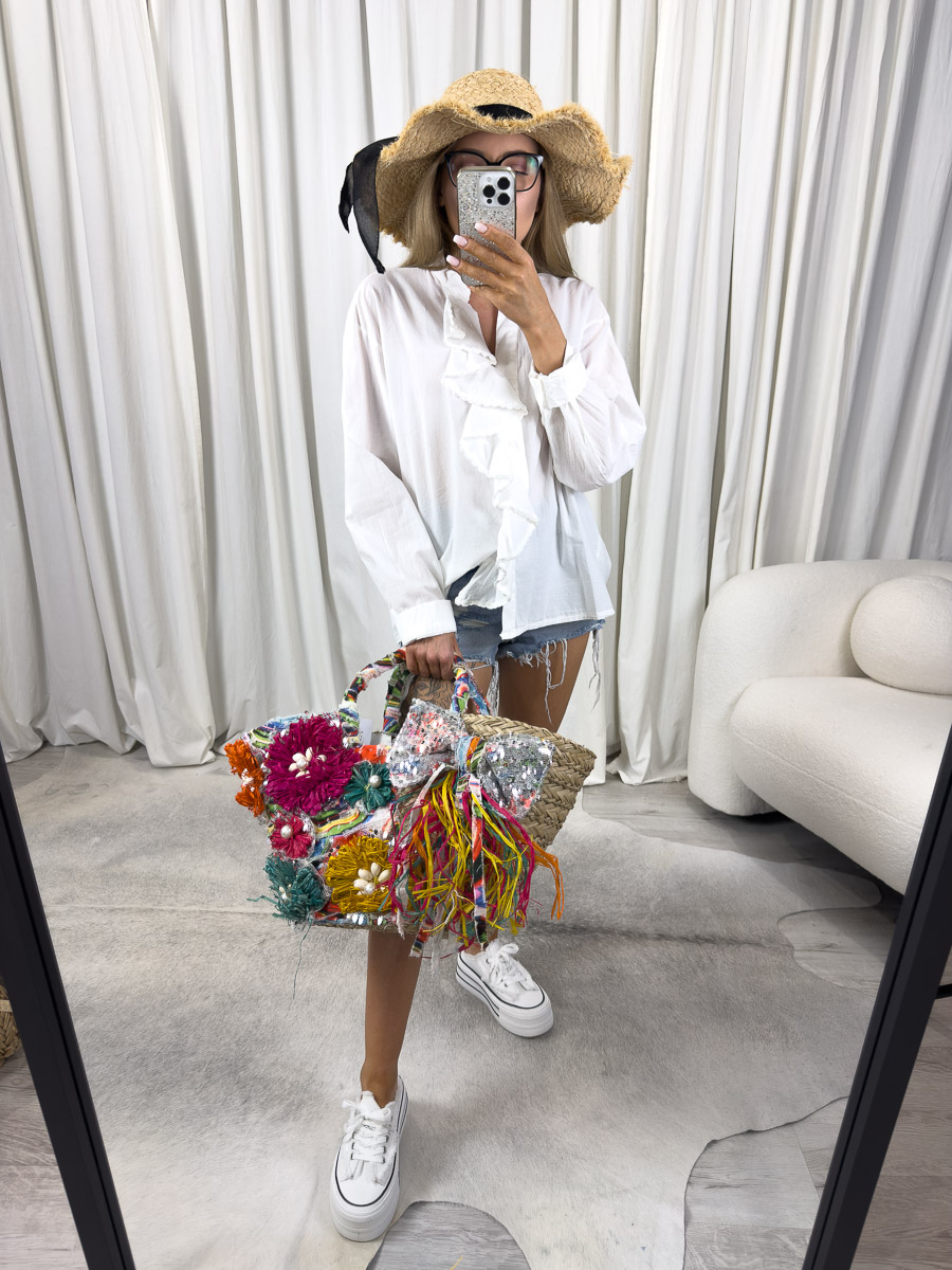 Zdjęcie produktowe sklepu internetowego z odzieżą damską – modelka w koszuli boho Vita Gioya z falbaną, szortami i wiklinową torbą z kwiatami