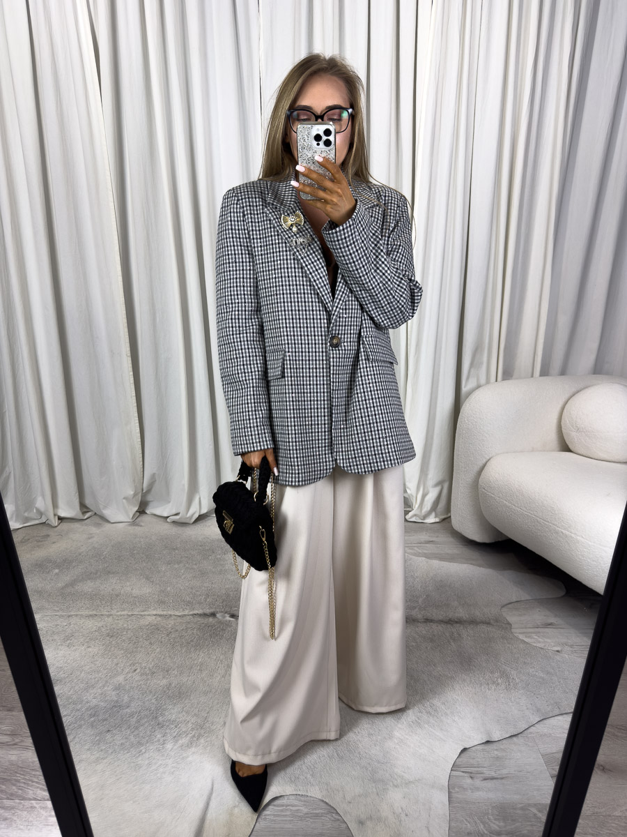 Modelka w marynarce o prostym kroju Glam z broszką i szerokimi spodniami. Zdjęcie produktowego sklepu internetowego z odzieżą damską.