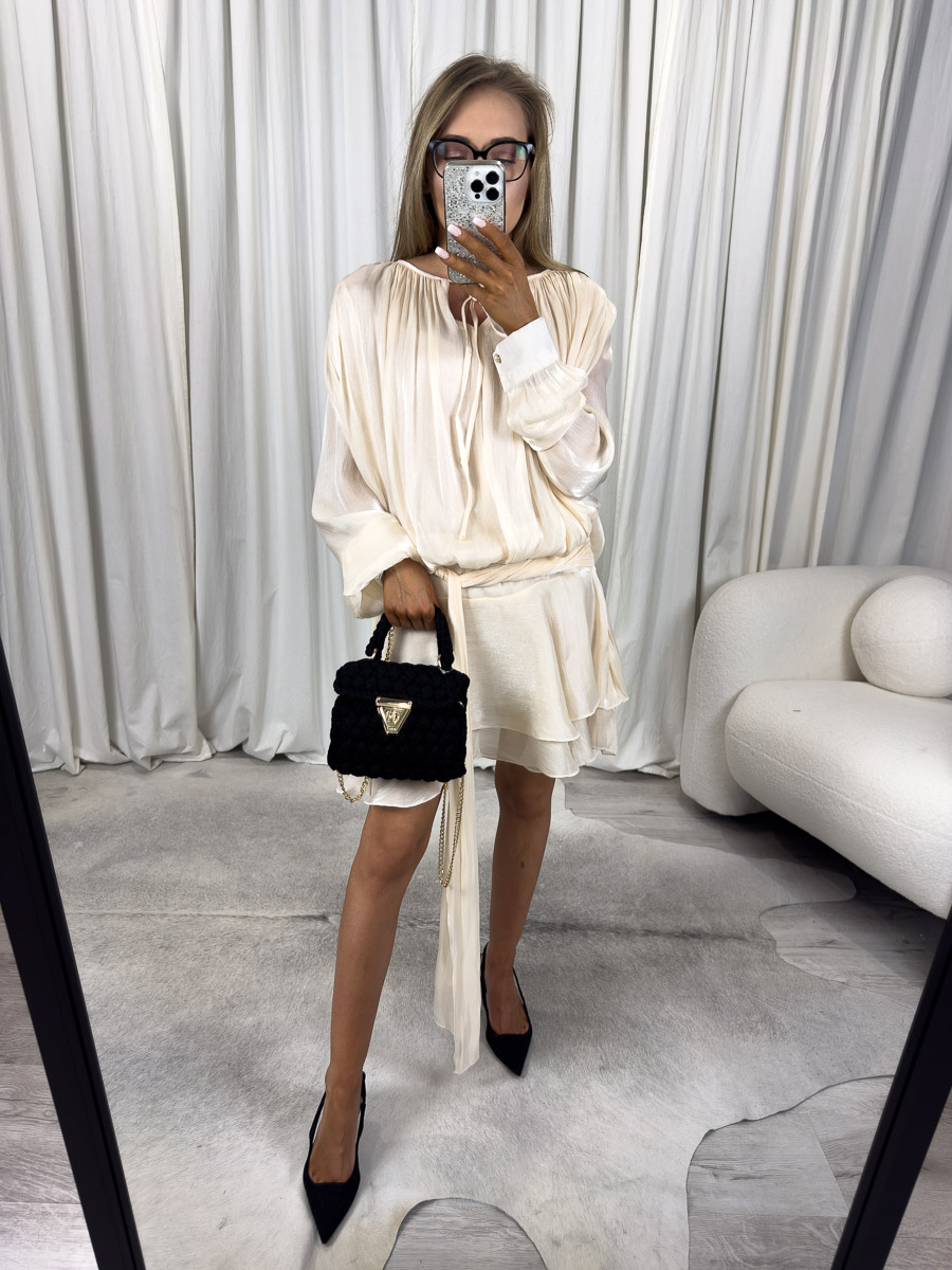 Modelka w kremowej sukience mini Satin z połyskiem, wiązaniem w talii i eleganckimi rękawami - zdjęcie produktowe do sklepu odzieżowego online.